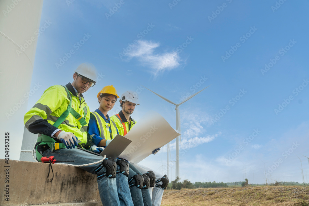 Team of female engineers and two foreman sit at the wind turbine station and talk holding blueprints work to inspect and repair wind turbines to produce electricity at the wind turbine station. Team of female engineers and two foreman sit at the wind turbine station and talk holding blueprints work to inspect and repair wind turbines to produce electricity at the wind turbine station.