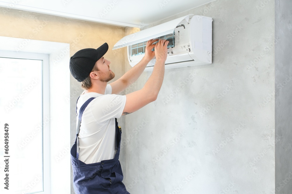 Smiling young male electrician repair conditioner in client home. Man mechanic or repairman fix filters in air condition device at customer house Smiling young male electrician repair conditioner in client home. Man mechanic or repairman fix filters in air condition device at customer house