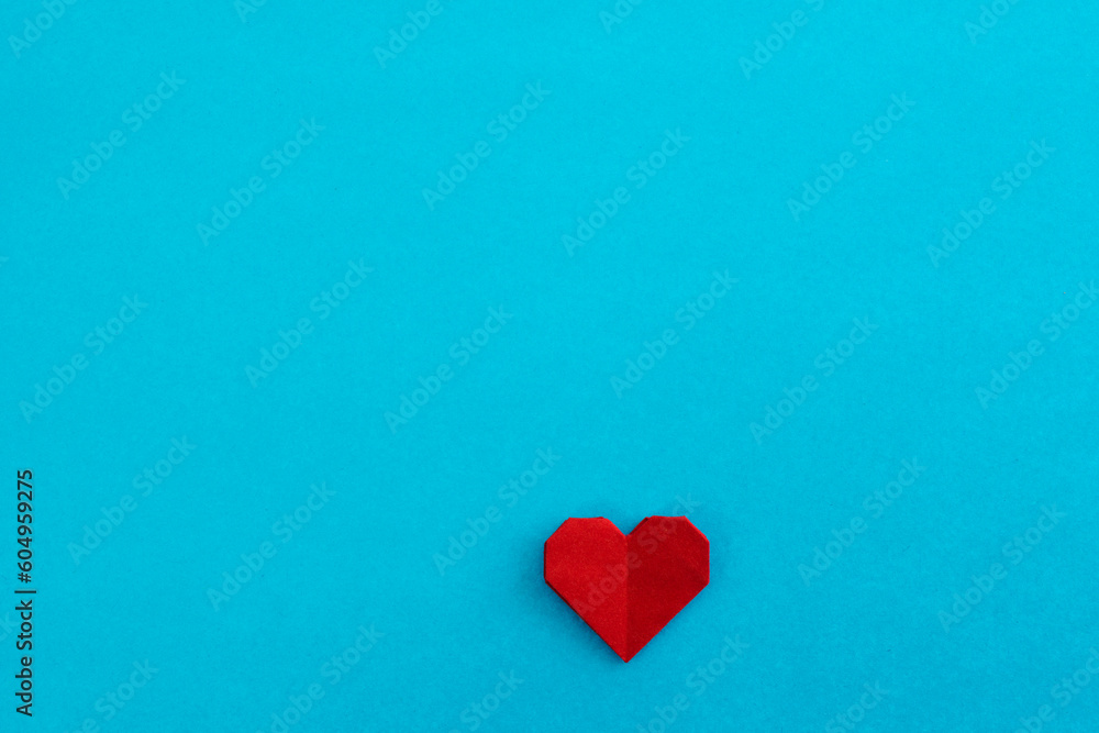 Red origami heart on blue background