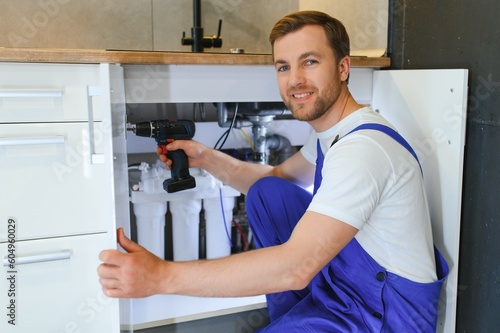 Repairman In Overalls Repairing Cabinet Hinge In Kitchen