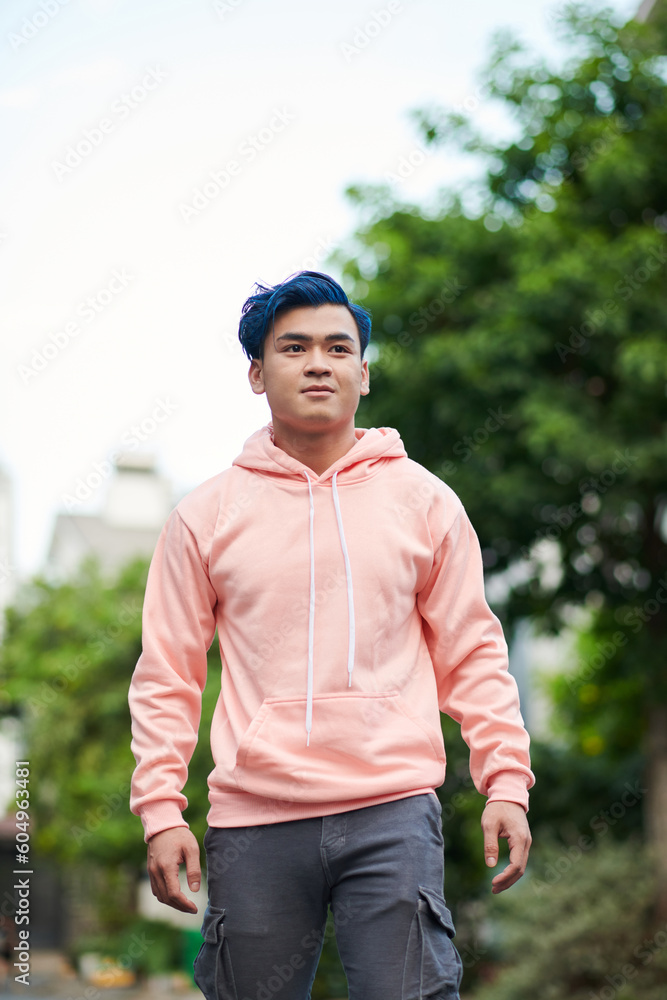 Positive teenage boy in salmon color hoodie walking in the street on summer day Positive teenage boy in salmon color hoodie walking in the street on summer day