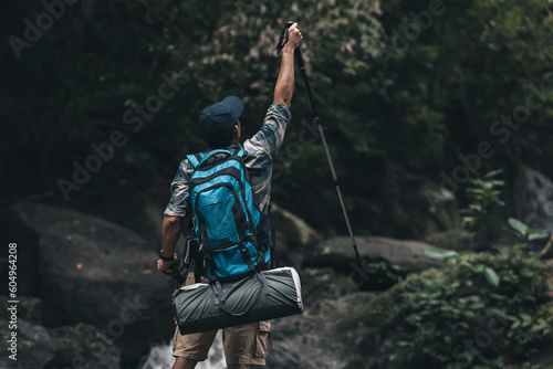 Hikers standing on the rock and raising hands to happy with backpacks and background waterfall in the forest. hiking and adventure concept.