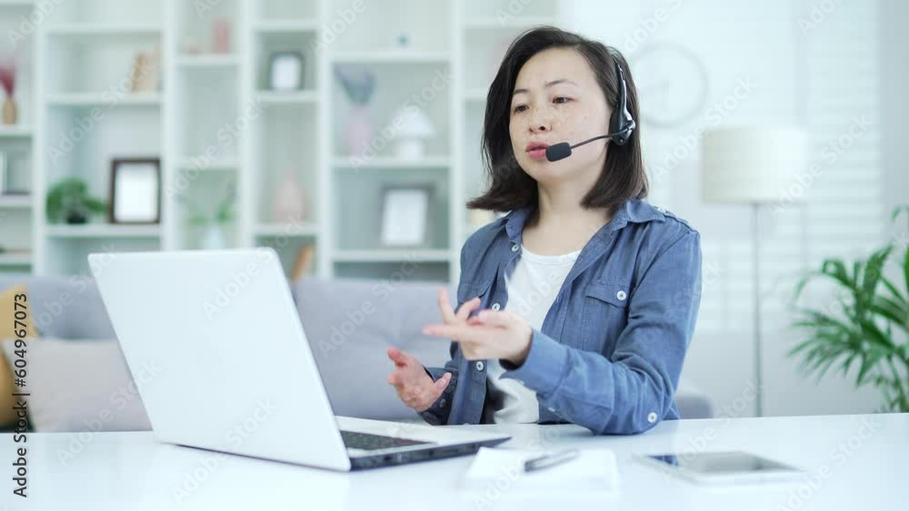 Confident asian woman in wireless headset talking on video call using laptop while sitting in home office. A female psychologist conducts an online consultation, communicates remotely with a patient Confident asian woman in wireless headset talking on video call using laptop while sitting in home office. A female psychologist conducts an online consultation, communicates remotely with a patient