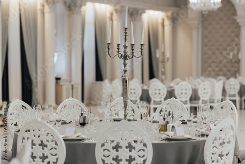 Tables setting up for wedding. Interior of restaurant for wedding dinner, ready for guests. Decorated with candles. Dishes, wine glasses and napkins.	
