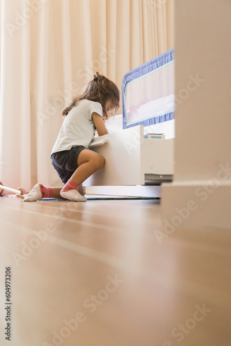 Small Caucasian girl playing in her bedroom, and opening drawers to explore and discover what's inside. Concept of curiosity, discovery, explore. Copy space