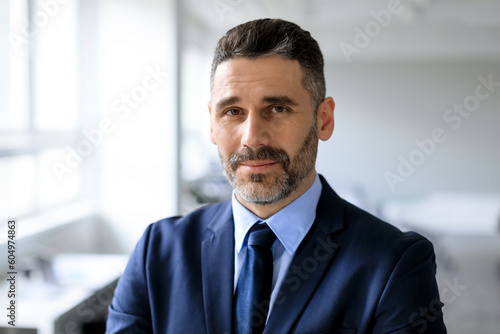 Closeup portrait of bearded middle aged businessman posing at office, man manager in suit and tie looking at camera