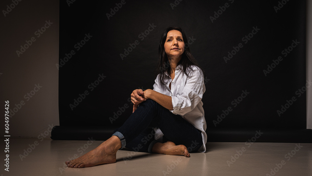 business portrait of a young girl about 40 years old, cute, emotional thoughtful, sitting on the floor on a dark background, indoor, reflected light, shot with copy space business portrait of a young girl about 40 years old, cute, emotional thoughtful, sitting on the floor on a dark background, indoor, reflected light, shot with copy space