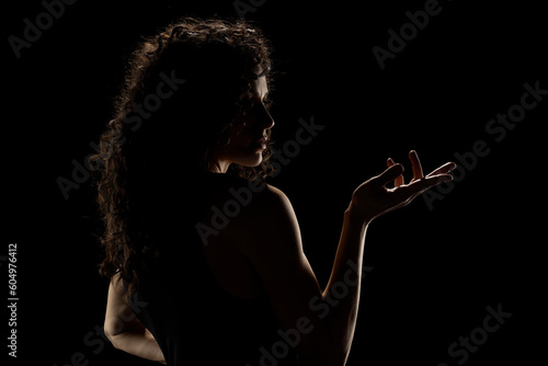 Sensual portrait silhouette of beautiful curly woman with outstretched hand in backlight on a black studio background