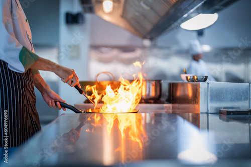 Chef in restaurant kitchen at stove and pan cooking flambe on food