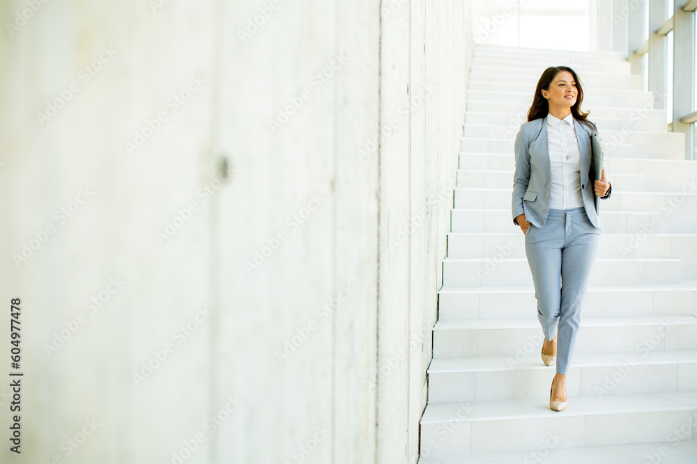Young business woman walking down the stairs and holding laptop - obrazy, fototapety, plakaty 