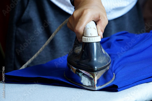 A housewife is using an old electric iron to flatten her trousers, which is a daily task.