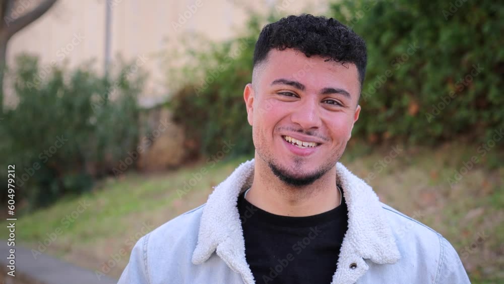 Close up portrait of happy young man smiling and looking at camera. Front view of male teenager standing outdoors at university campus. Student guy laughing at high school. Youngster person face. High Close up portrait of happy young man smiling and looking at camera. Front view of male teenager standing outdoors at university campus. Student guy laughing at high school. Youngster person face. High
