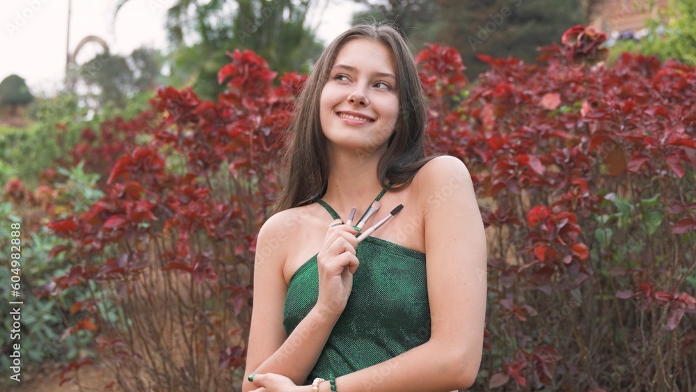 Young woman in a green dress holding cosmetics in front of flowers Young woman in a green dress holding cosmetics in front of flowers