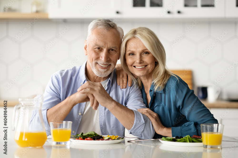 Portrait of happy mature couple posing in kitchen while eating lunch together