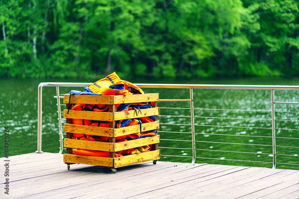 Fototapeta premium Orange life jackets in a wooden box on the pier by the river