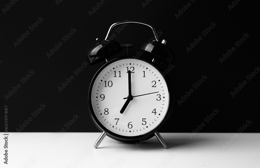 Naklejka premium Black alarm clock on white table on black background.