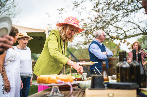 Smiling beautiful senior woman holding food for party, preparing a lunch and an outdoor party in the garden, healthy and happy elderly people concept photo