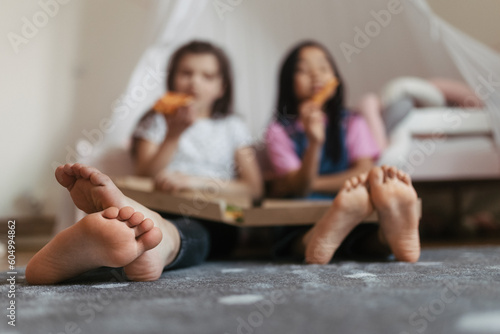 Friends sit on the floor with pizza box in their lap.
