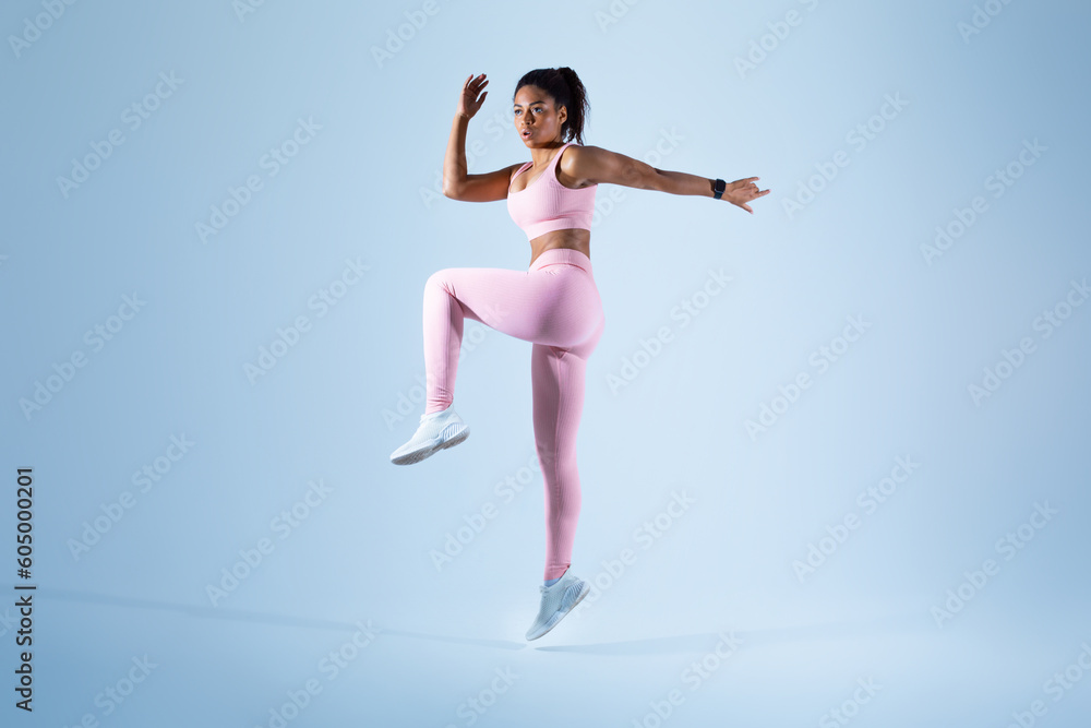 Young black woman in sportswear jogging and jumping looking at copy space, sprinting on blue background, full length