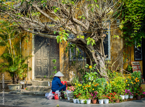 A side view of Vietnamese woman covered by a rice hat working near beautiful flowers at Hoi An old town in a sunny day.