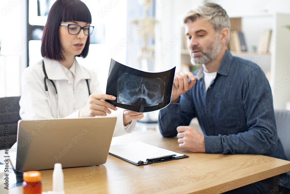 Skilled radiologist in white uniform and eyeglasses explaining visible ...