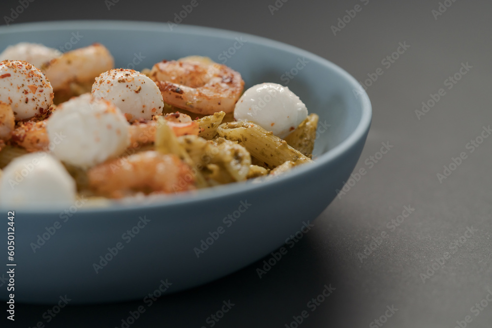 Penne pasta with shrimps and mozzarella and pesto in blue bowl with copy space