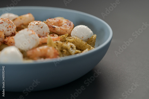 Penne pasta with shrimps and mozzarella and pesto in blue bowl with copy space