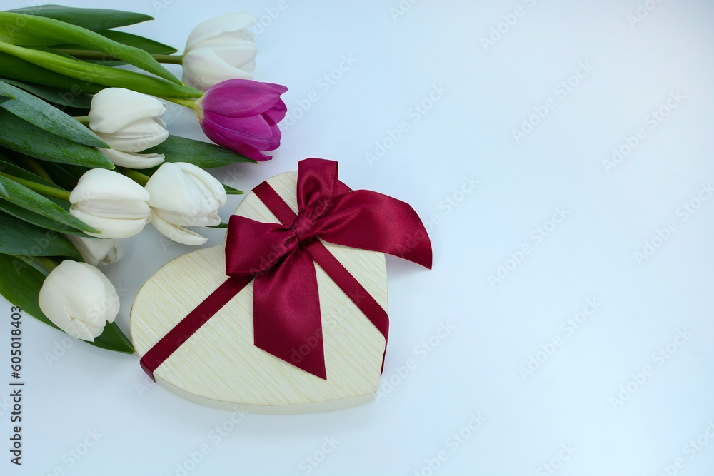 Gift box in the shape of a heart and a bouquet of white and purple tulips on a light background. Mother's day, Valentine's day, birthday celebration concept. Postcard. Copy space for text, top view Gift box in the shape of a heart and a bouquet of white and purple tulips on a light background. Mother's day, Valentine's day, birthday celebration concept. Postcard. Copy space for text, top view
