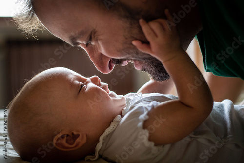 side view of father face watching his newborn baby in white top laying on the bed
