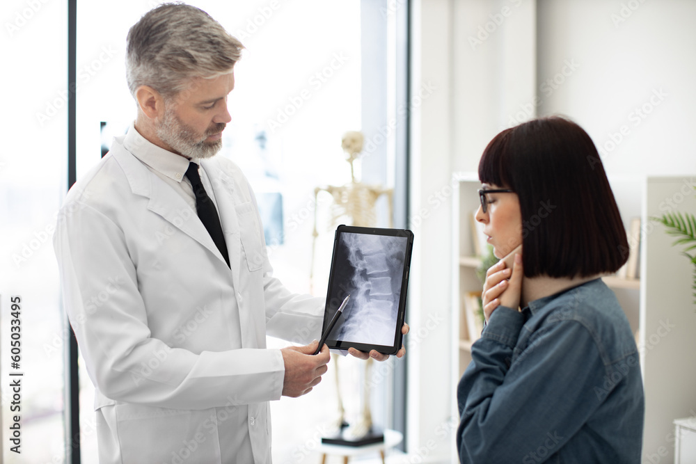Female brunette talking about discomfort under C collar while male physician explaining cause of pain using tablet. Efficient professional diagnosing neck injury using CT scan report in clinic.