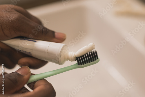 Slika na platnu African american male hand holding toothbrush with toothpaste applied on it in bathroom
