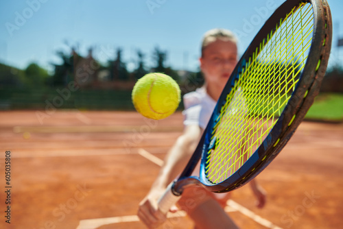 Close up photo of a young girl showing professional tennis skills in a competitive match on a sunny day, surrounded by the modern aesthetics of a tennis court. © .shock