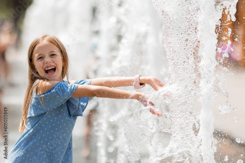 little happy girl is playing in the fountain on a sunny summer day