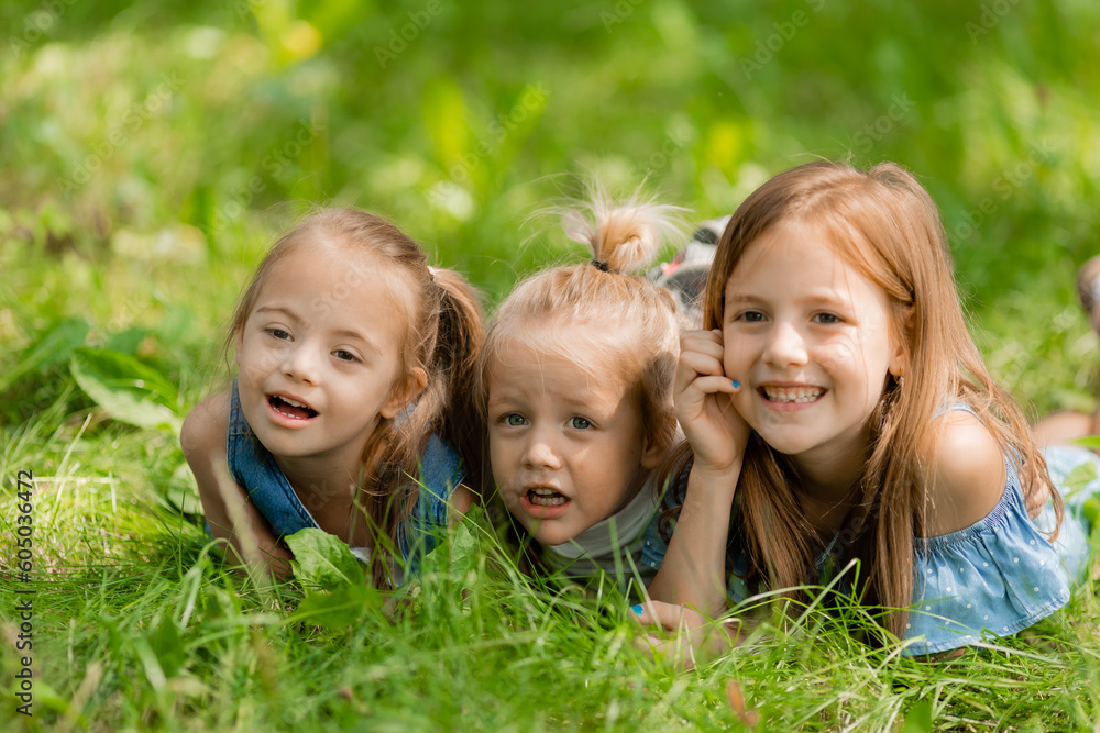 three small children lie in the green grass in summer. Happy childhood. A child with down syndrome three small children lie in the green grass in summer. Happy childhood. A child with down syndrome