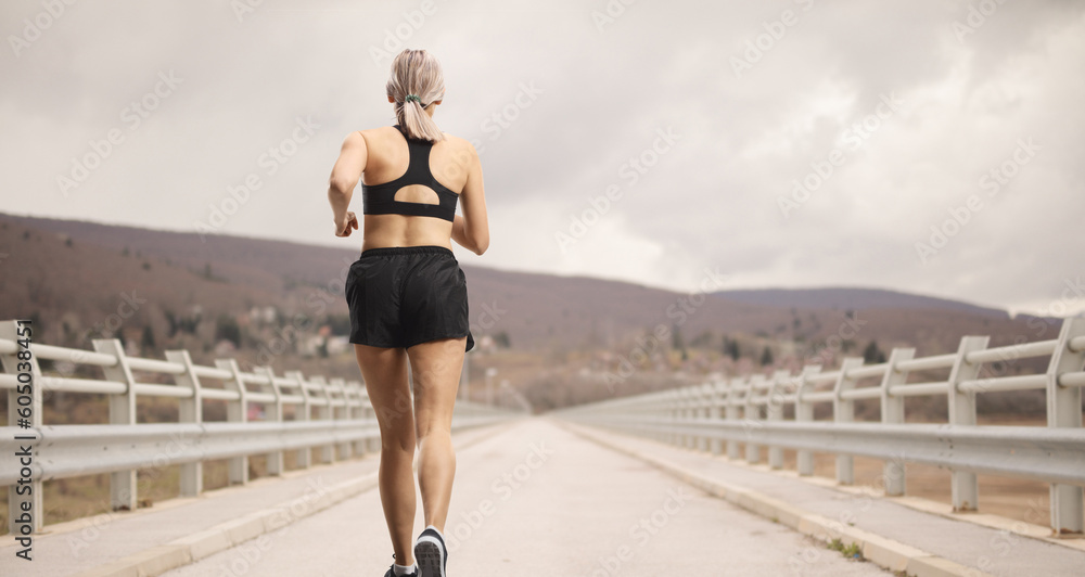 Rear shot of a woman in sportswear running at a bridge
