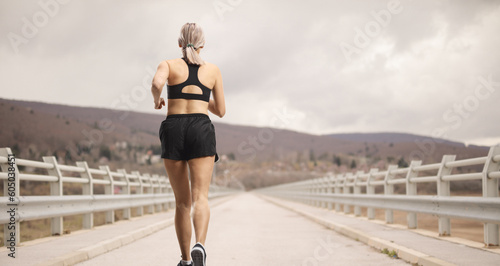 Rear shot of a woman in sportswear running at a bridge © Ljupco Smokovski