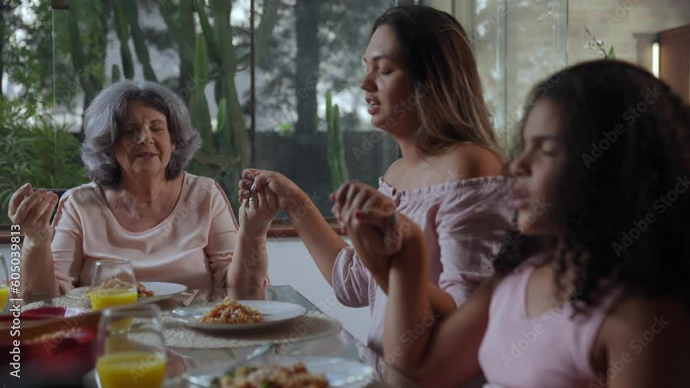 brazilian grandmother mother and daughter sitting at the dinner table holding hands praying before mother's day lunch brazilian grandmother mother and daughter sitting at the dinner table holding hands praying before mother's day lunch