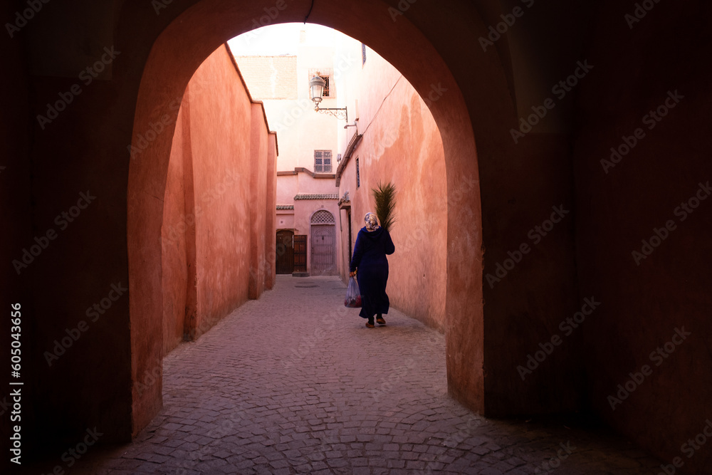 Woman walking with a bunch of flowers through the moorish arches in the streets of the Marrakech Medina