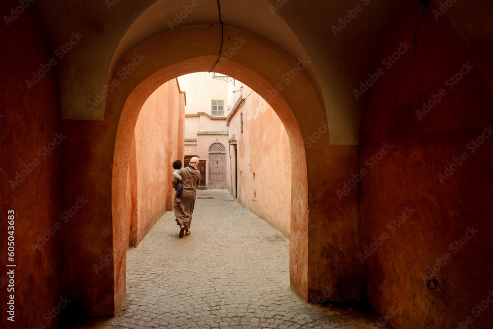 Obraz premium Woman walking with a baby through the moorish arches in the streets of the Marrakech Medina