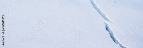 Crack in the ice cover. Snow covered ice. Cracked ice floes on the sea in the Arctic. Polar region. Snow texture. Wide panoramic texture for background and design.