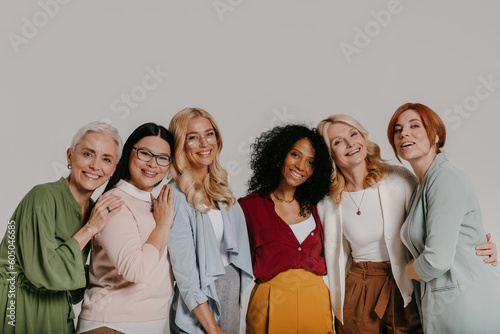 Multi-ethnic group of elegant mature women bonding and smiling against grey background