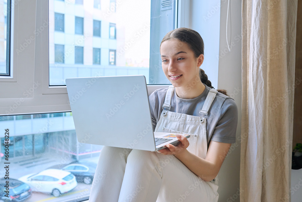 Teenage girl sitting on a windowsill using a laptop Teenage girl sitting on a windowsill using a laptop