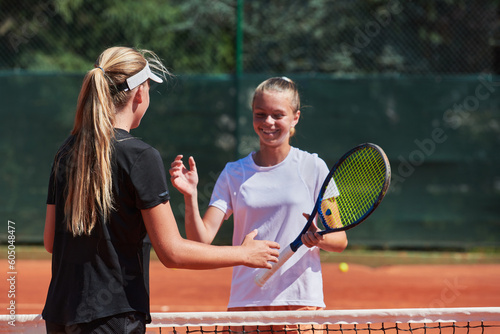 Two female tennis players shaking hands with smiles on a sunny day, exuding sportsmanship and friendship after a competitive match. © .shock