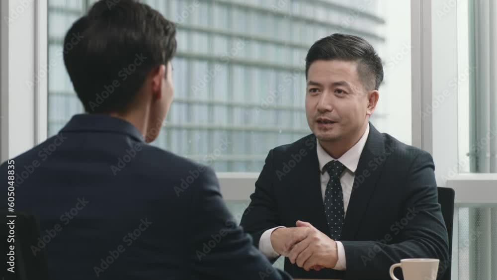 two asian corporate executives sitting at desk having a business discussion shaking hands in modern office two asian corporate executives sitting at desk having a business discussion shaking hands in modern office