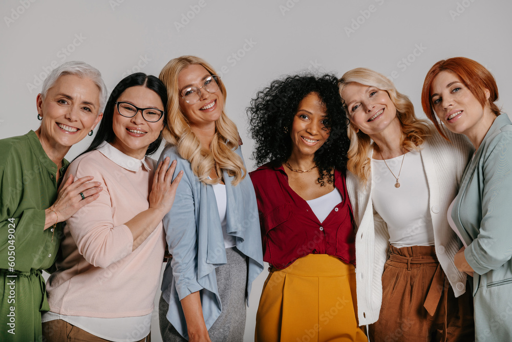Multi-ethnic group of beautiful mature women bonding and smiling against grey background Multi-ethnic group of beautiful mature women bonding and smiling against grey background