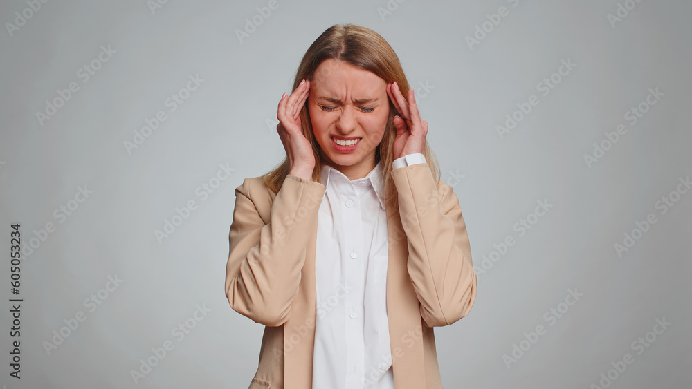 Business woman in formal office suit rubbing temples to cure headache problem, suffering from tension, migaine, stress, grimacing in pain, high blood pressure isolated alone on gray wall background Business woman in formal office suit rubbing temples to cure headache problem, suffering from tension, migaine, stress, grimacing in pain, high blood pressure isolated alone on gray wall background