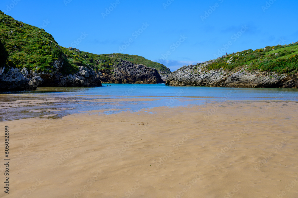 View on Playa de Poo during low tide near Llanes, Green coast of Asturias, North Spain with sandy beaches, cliffs, hidden caves, green fields and mountains.
