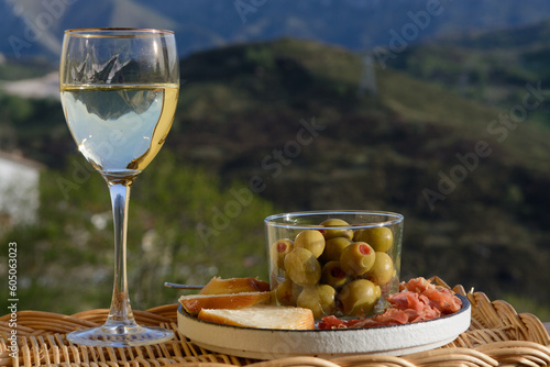 Glasses of dry white wine and spanish tapas olives in bowl with mountains peaks on background in sunny day