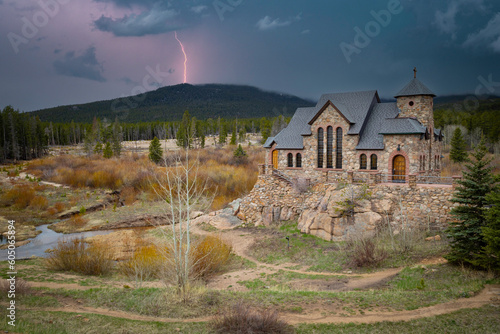 St. Catherine's of Siena Chapel on the Rock in Allenspark, CO, under a stormy sky with a lightning bolt behind the mountain.