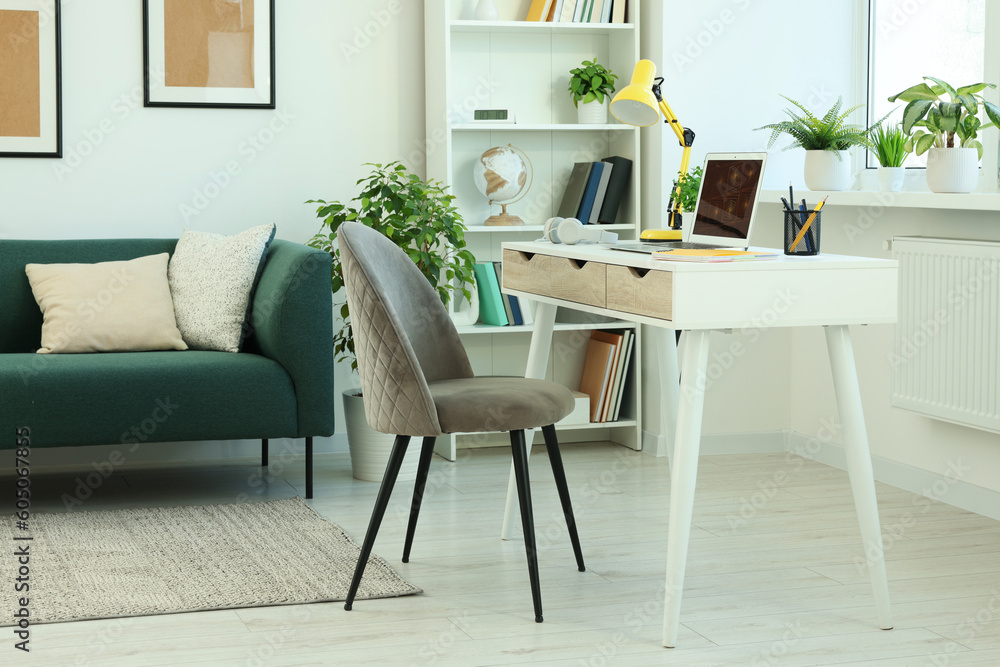 Fototapeta premium Cozy workspace with modern laptop on white wooden desk and comfortable chair at home